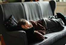 “끊이지 않는 피로, 나만의 루틴 찾기가 핵심” woman in pink jacket lying on gray couch