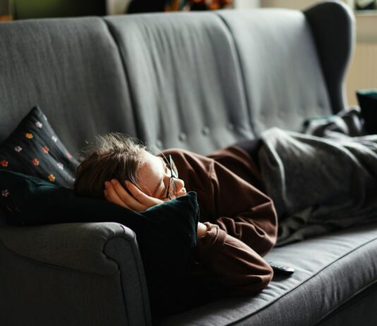 “끊이지 않는 피로, 나만의 루틴 찾기가 핵심” woman in pink jacket lying on gray couch